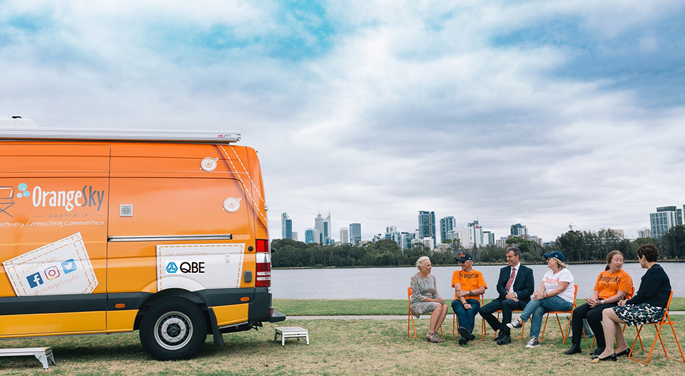 Group of volunteers sitting on ornage chairs next to an Orange Sky and QBE branded van